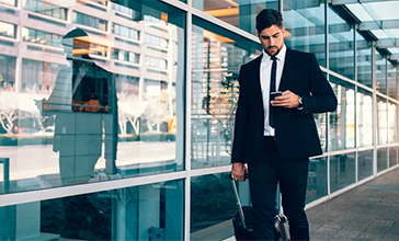 Business man pulling his carry-on luggage using his mobile phone